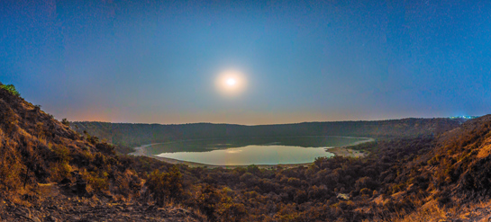 The moon sparkles in the night sky as it lights up the Lonar crater below. The impact crater was formed around 50,000 years ago when a meteor hit the earth. Today, it cradles a lake at the center and a dense forest along the rim.