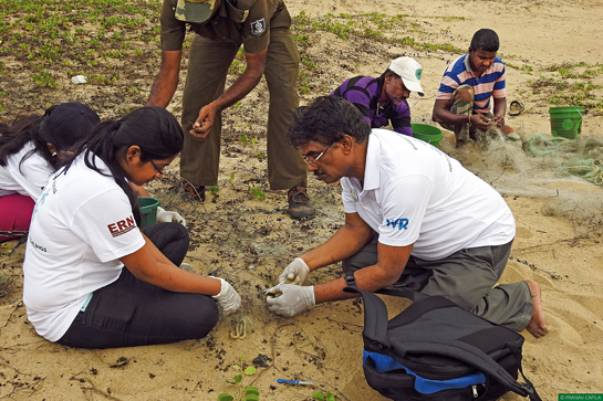 Veterinarian Dr. Indramani Nath shows his students how to untangle a hatchling from a ghost net. Forest guards and local volunteers can be seen working in the background.